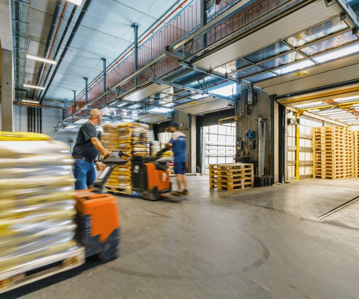 Lagerhalle mit Futterpaletten, Mitarbeiter verladen Ware mit Hubwagen